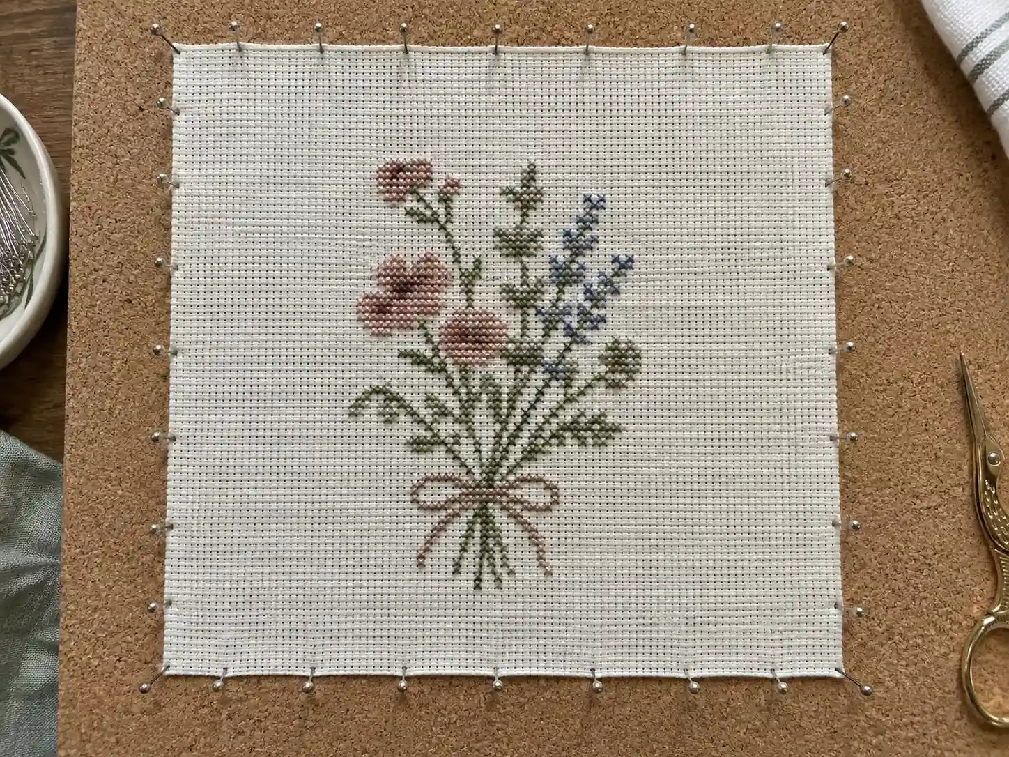 A finished cross-stitch piece pinned out square on a blocking board