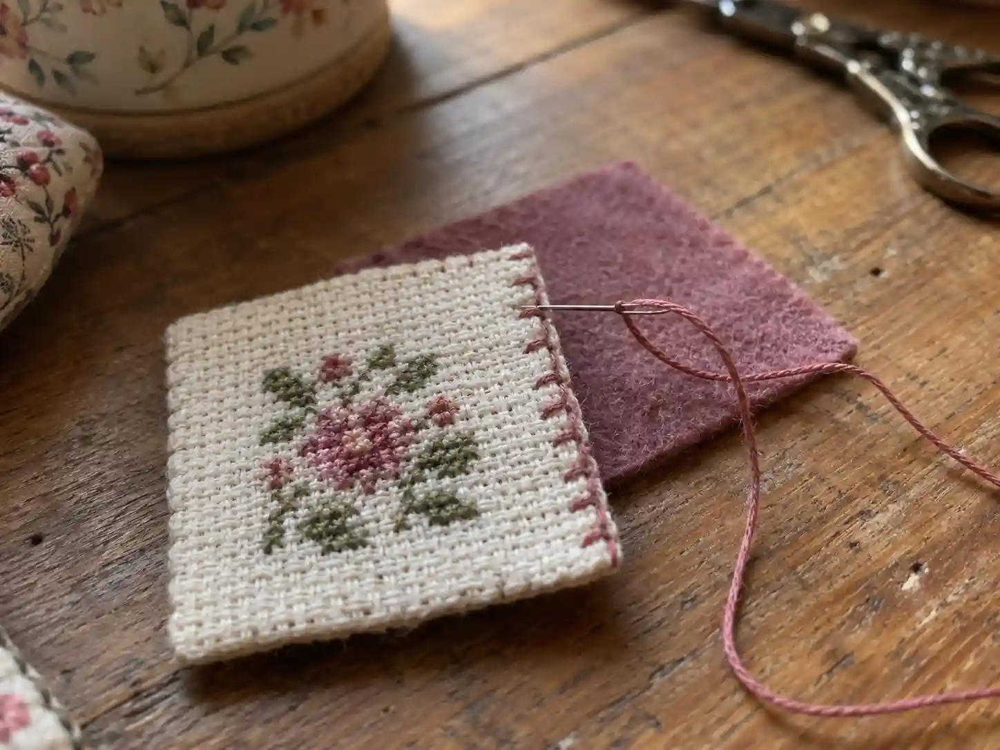 A finished cross-stitch piece being sewn into a felt-backed pouch