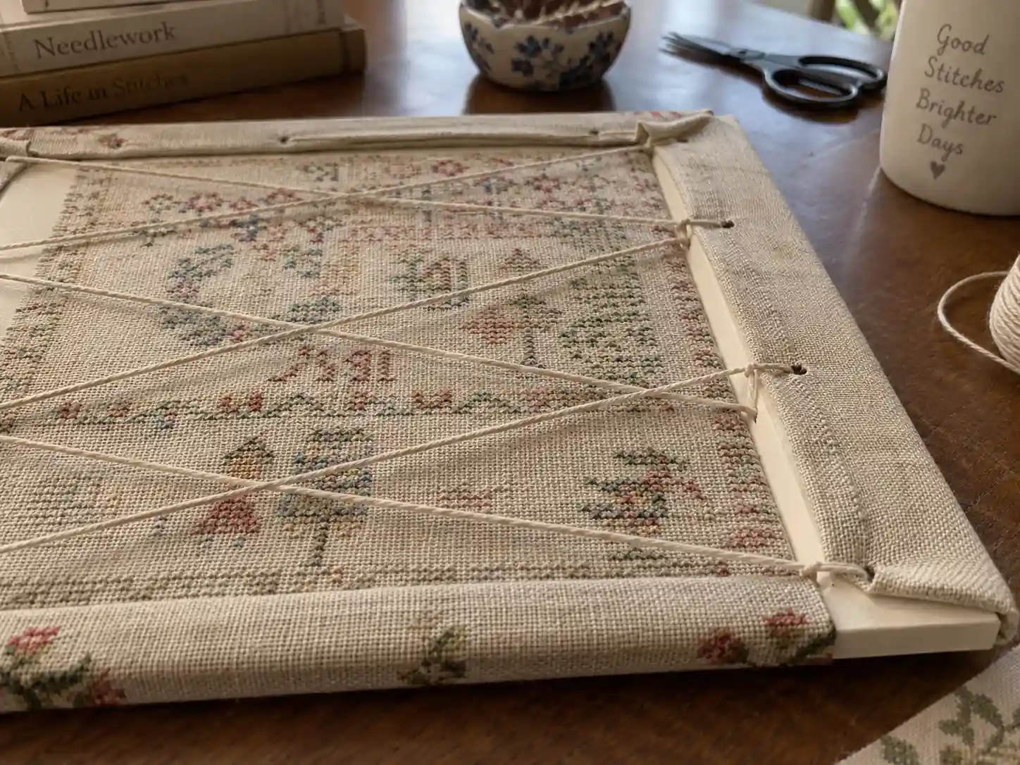 A finished cross-stitch piece being laced onto a mounting board ready for framing